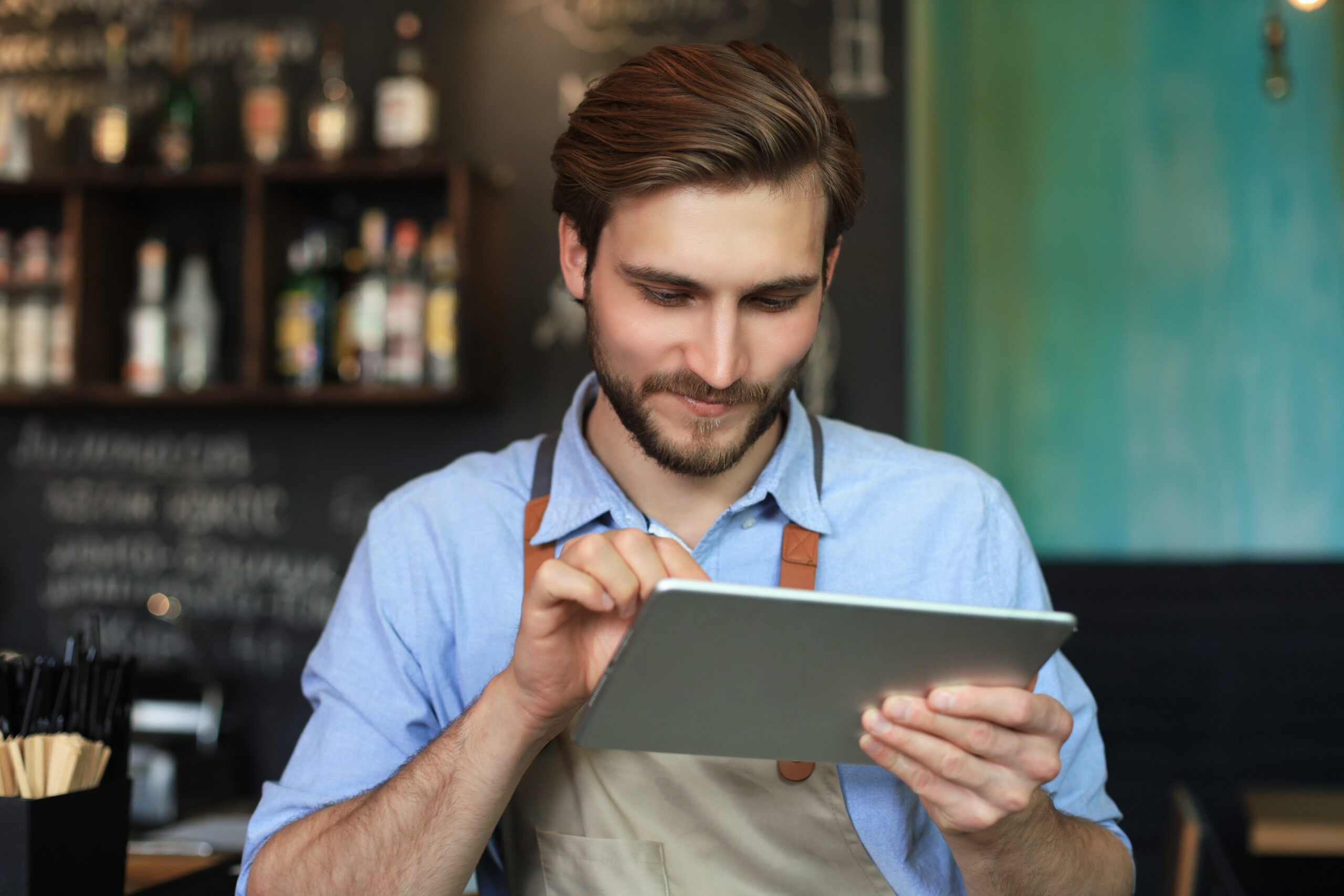 Young male owner using digital tablet while standing in cafe.